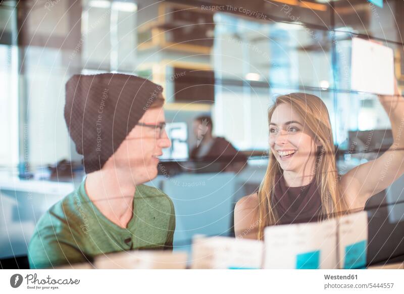 Junger Mann und Frau arbeiten zusammen in einem Büro Gemeinsam Zusammen Miteinander Kollegen Arbeitskollegen Brainstorming Ideenfindung Glasscheibe Glasscheiben