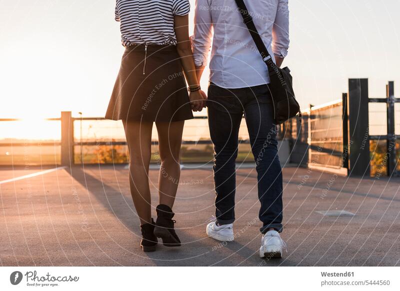 Junges Paar geht bei Sonnenuntergang Hand in Hand auf der Parkebene gehen gehend Sonnenuntergänge Parkdeck Parkdecks Pärchen Paare Partnerschaft Stimmung