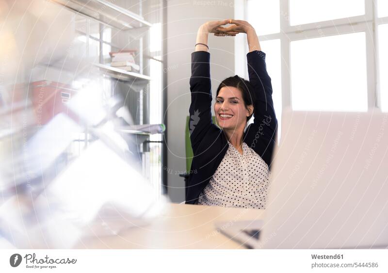 Glückliche Geschäftsfrau sitzt im Büro, schaut auf den Laptop, streckt sich glücklich glücklich sein glücklichsein sitzen sitzend Notebook Laptops Notebooks