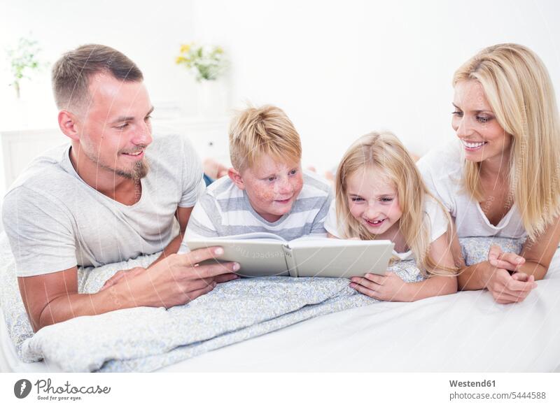 Familie liegt im Bett und liest gemeinsam ein Buch Bücher Familien lächeln lesen Lektüre Betten Mensch Menschen Leute People Personen Zuhause zu Hause daheim
