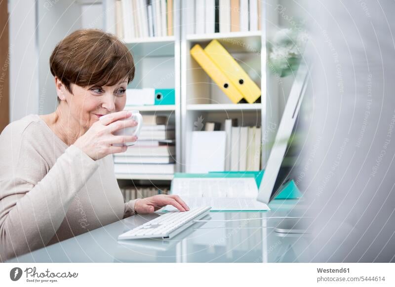 Ältere Frau arbeitet am Computer mit einer Tasse Kaffee weiblich Frauen arbeiten Arbeit trinken sitzen sitzend sitzt lernen Seniorin älter Seniorinnen alt