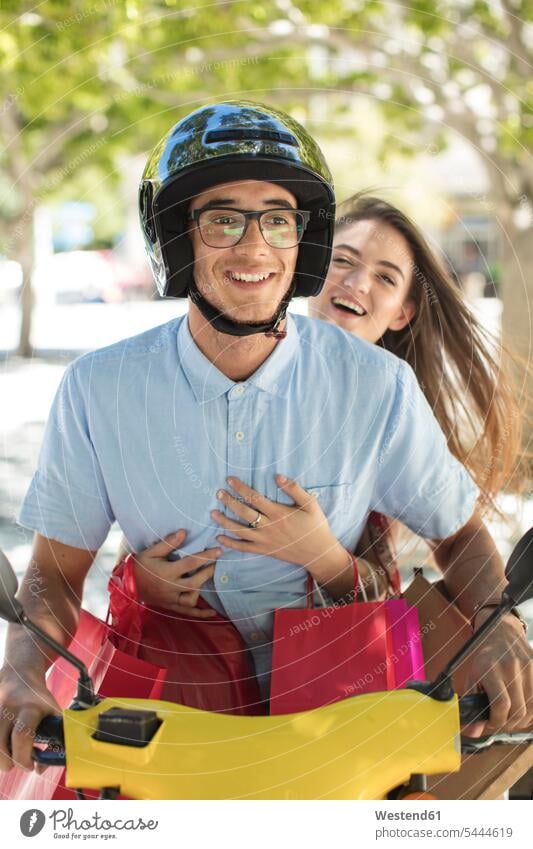 Glückliches junges Paar mit Einkaufstaschen auf Motorroller Roller Piaggio Pärchen Paare Partnerschaft glücklich glücklich sein glücklichsein fahren