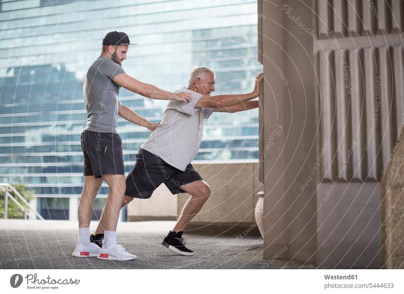 Fitnesstrainer, der einen älteren Mann bei einer Dehnungsübung anleitet Trainer Uebungsleiter Übungsleiter dehnen strecken Sportler Senior ältere Männer