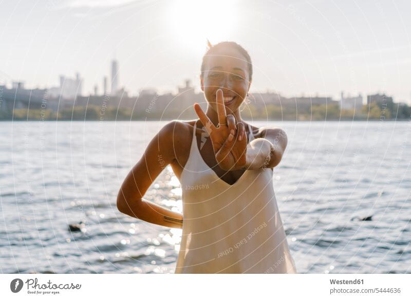 Junge Frau in Brooklyn steht am East River und gibt Siegeszeichen weiblich Frauen Victory-Zeichen V Zeichen Victory Zeichen Freude freuen Unbeschwert Sorglos