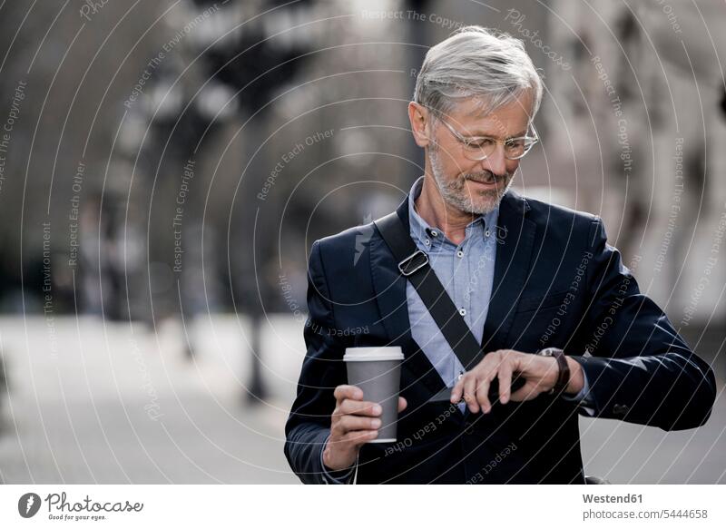 Grauhaariger Geschäftsmann in der Stadt schaut auf die Uhr und hält Kaffee zum Mitnehmen Handy Mobiltelefon Handies Handys Mobiltelefone Businessmann