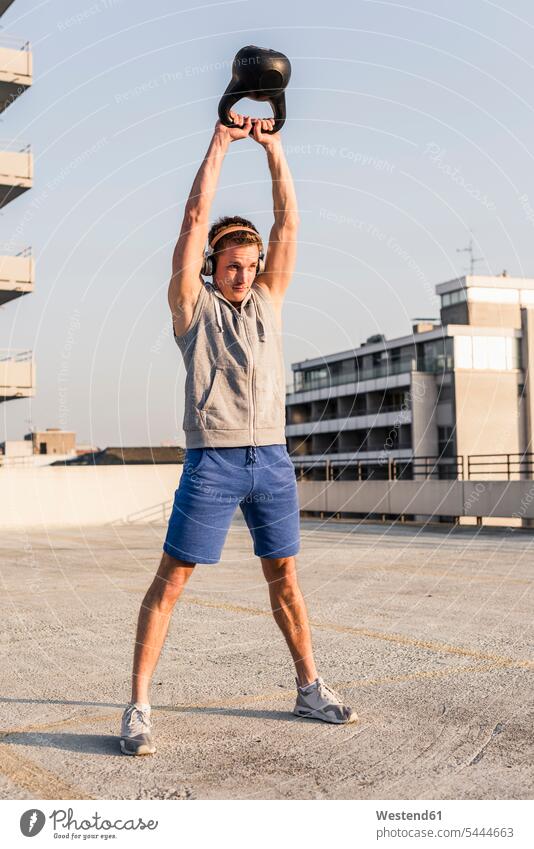 Junger Mann übt mit Kesselglocke auf einem Dach jung fit Gewicht Gewichte Rundgewicht Kettlebell Kugelhantel Kettlebells Kraft stark Stärke kräftig Training