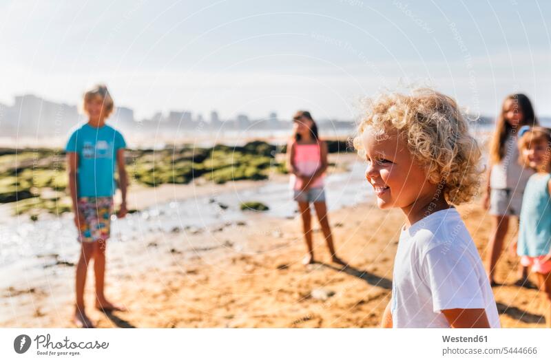 Glücklicher kleiner Junge am Strand mit anderen Kindern im Hintergrund Beach Straende Strände Beaches schauen schauend anschauen betrachten Buben Knabe Jungen