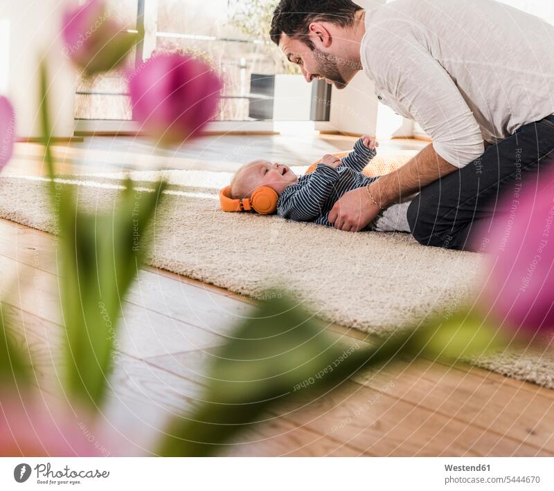 Vater spielt mit Baby Sohn mit Kopfhörern Zuhause zu Hause daheim Papas Väter Vati Vatis Papis knuddeln umarmen Kind Babies Babys Kinder Eltern Familie Familien