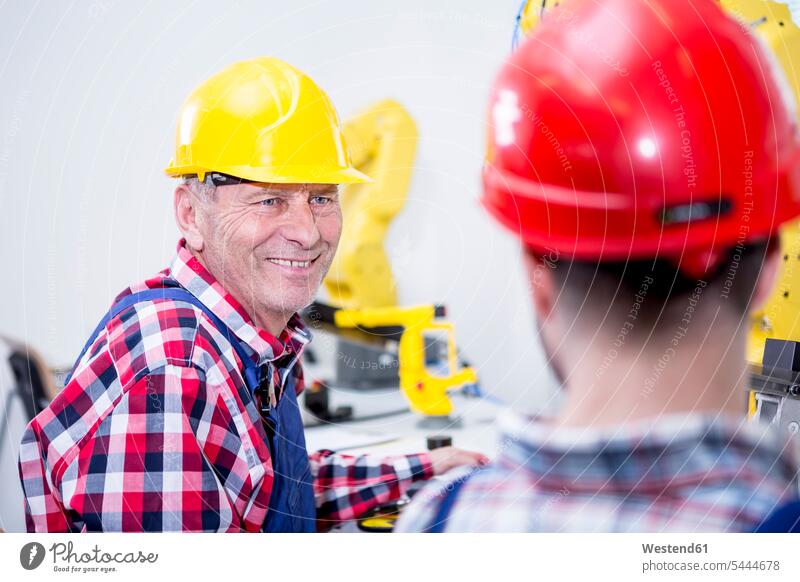 Mann in Fabrik mit Schutzhelm, der einen Kollegen anlächelt Fabriken Arbeitskollegen Industrie industriell Gewerbe Industrien herstellen produzieren Herstellung