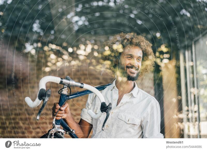 Lächelnder junger Mann mit Fahrrad lächeln Männer männlich Bikes Fahrräder Räder Rad Erwachsener erwachsen Mensch Menschen Leute People Personen Raeder