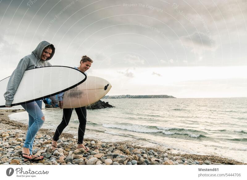 Glückliche Freunde mit Surfbrett am steinigen Strand spazieren Freundinnen Beach Straende Strände Beaches glücklich glücklich sein glücklichsein Surfbretter