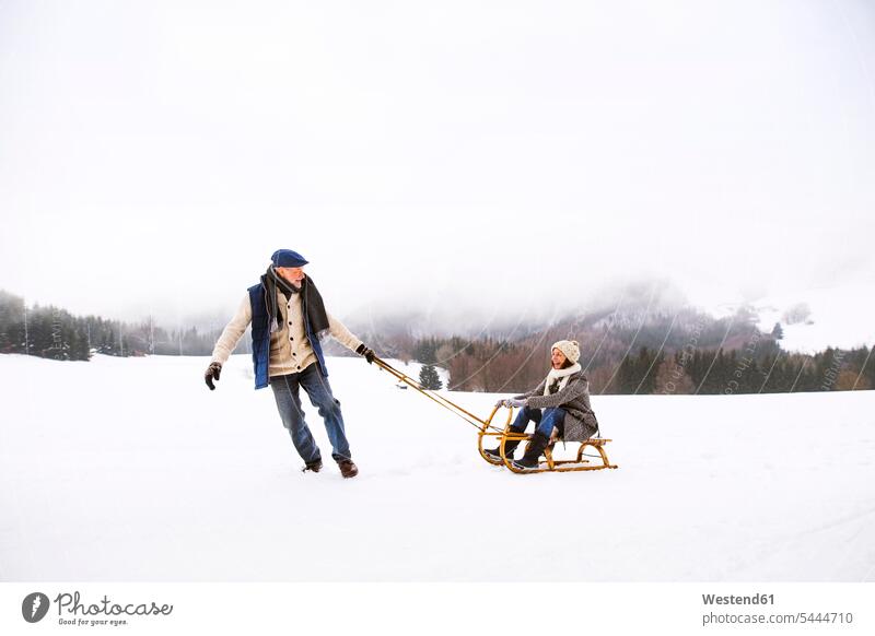 Älteres Ehepaar amüsiert sich mit Schlitten in verschneiter Landschaft Seniorenpaar älteres Paar Seniorenpaare ältere Paare Seniorenpärchen Erwachsenes Paar
