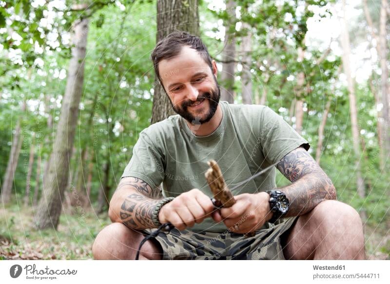 Lächelnder Mann beim Schnitzen im Wald Forst Wälder Männer männlich Messer lächeln Tattoo Tätowierungen Tatoos Taetowierung Tattoos Taetowierungen schnitzen