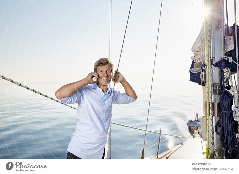 Porträt eines lächelnden reifen Mannes, der auf seinem Segelboot telefoniert Segeln segelnd segelt Portrait Porträts Portraits Männer männlich Bootsport