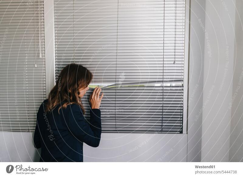 Frau steht am Fenster und spioniert durch Jalousien Rollo Rollos überwachen Beobachtung beobachten überprüfen spionieren weiblich Frauen zuschauen ansehen