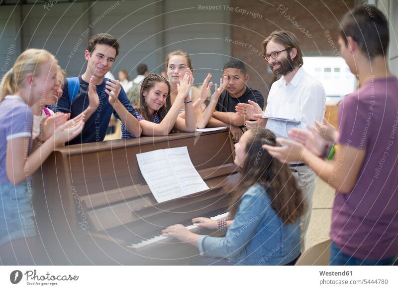 Lehrer mit einer Gruppe von Schülern steht um das Klavier herum und applaudiert klatschen lernen Tasteninstrument Musikinstrument Pädagoge Bildung Schule