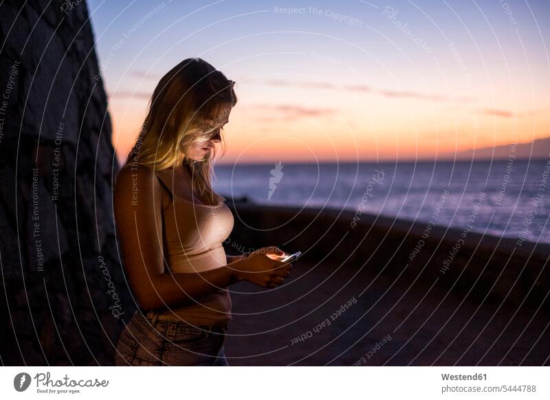 Frau benutzt Handy bei Sonnenuntergang Smartphone iPhone Smartphones benutzen benützen Meer Meere weiblich Frauen Sonnenuntergänge Mobiltelefon Handies Handys