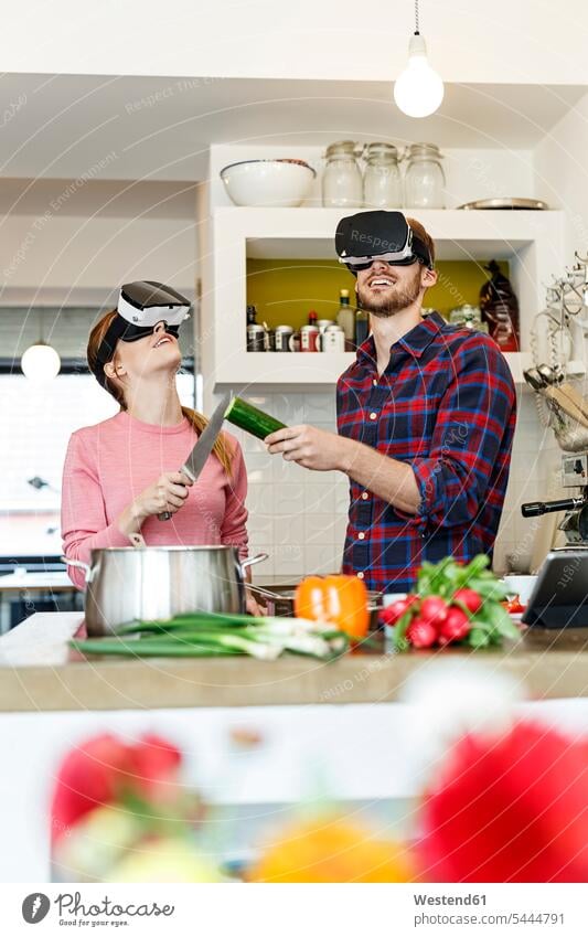 Glückliches junges Paar mit VR-Brille kocht gemeinsam in der Küche Virtuelle Realität Virtuelle Realitaet kochen Gemeinsam Zusammen Miteinander Pärchen Paare