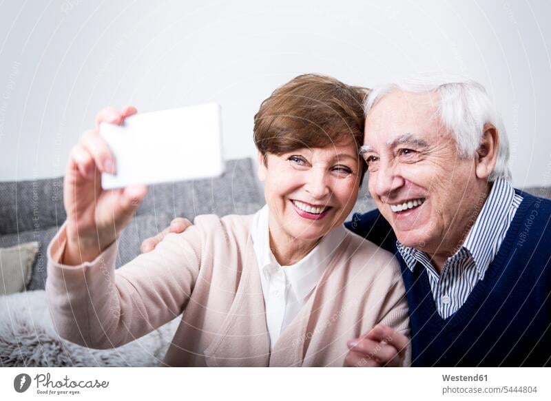 Älteres Paar sitzt auf der Couch und macht ein Smartphone-Selfie Deutschland iPhone Smartphones Selbstportrait Selfies sich selbst fotografieren Anruf