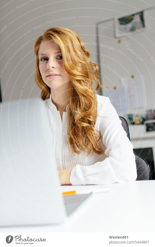 Porträt einer lächelnden jungen Frau mit Laptop am Schreibtisch im Büro Geschäftsfrau Geschäftsfrauen Businesswomen Businessfrauen Businesswoman Office Büros