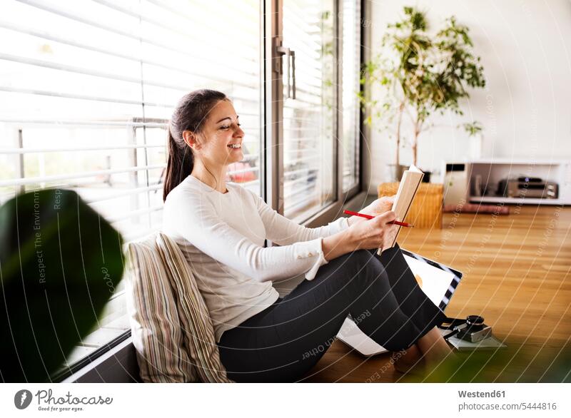 Lachende Frau, die zu Hause arbeitet weiblich Frauen Erwachsener erwachsen Mensch Menschen Leute People Personen Heft Hefte lachen sitzen sitzend sitzt arbeiten