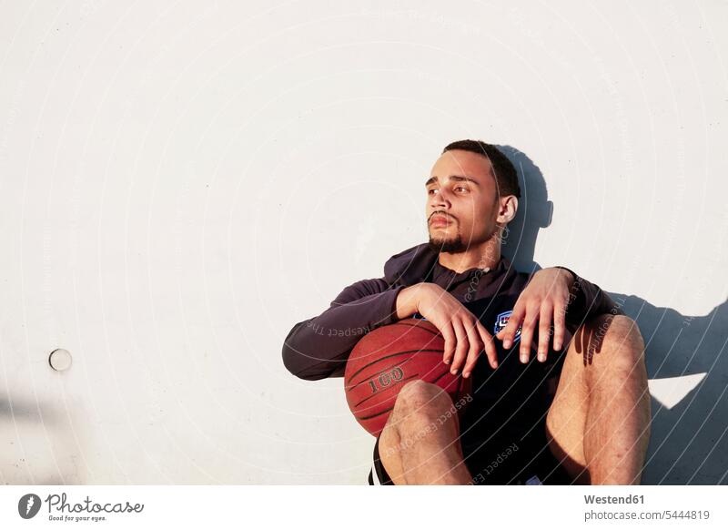 Junger Mann mit Basketball in der Pause ausruhen Rast Erholung erholen Basketbaelle Basketbälle Männer männlich sitzen sitzend sitzt trainieren Sport