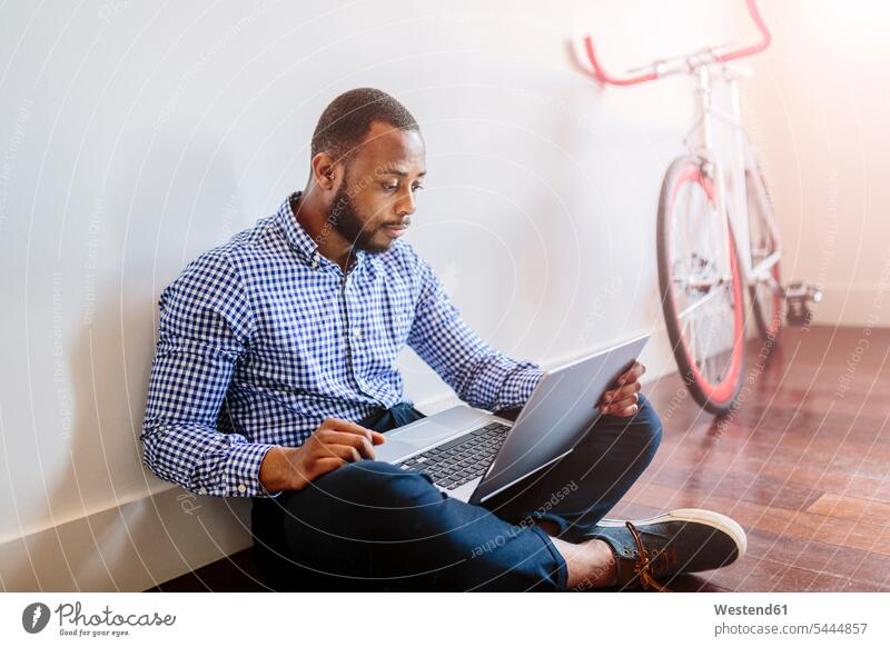 Mann mit Laptop auf Holzboden sitzend mit Fahrrad im Hintergrund Geschäftsmann Businessmann Businessmänner Geschäftsmänner Notebook Laptops Notebooks sitzt