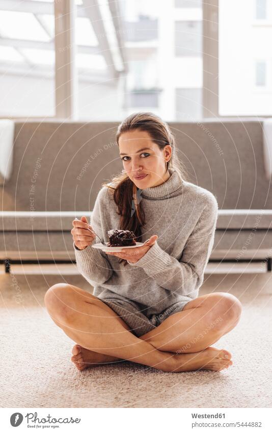 Porträt einer Frau, die auf dem Boden sitzt und ein Stück Kuchen isst sitzen sitzend lächeln essen essend weiblich Frauen Süßspeise Süsses Süßes süß Süßspeisen