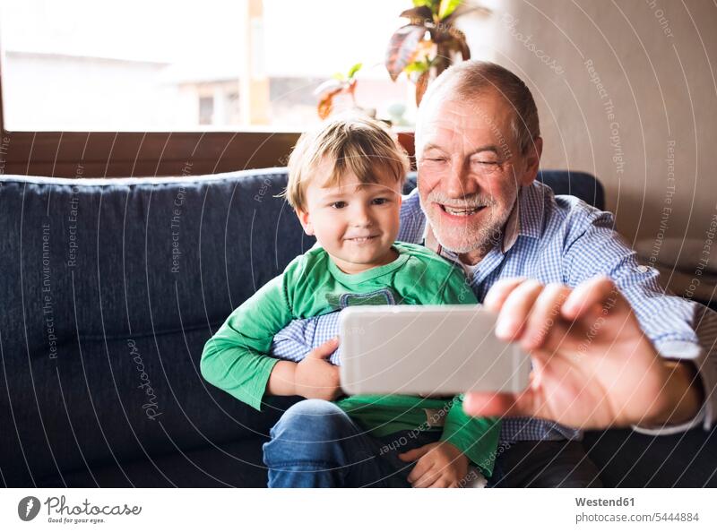 Großvater und Enkel sitzen auf der Couch und machen Smartphone-Selfies Teilen Sharing spielen fotografieren Opa Großpapa Großpapas Opas Opi Großväter Opis