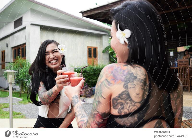 Zwei glückliche Frauen stoßen im Garten mit Cocktails an Portrait Porträts Portraits Glück glücklich sein glücklichsein Freundinnen weiblich Longdrink