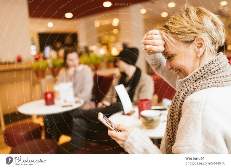 Junge glückliche Frau benutzt Smartphone in einem Cafe lächeln Drahtlose Technologie drahtlose Verbindung Drahtlose Kommunikation schnurlose Verbindung weiblich