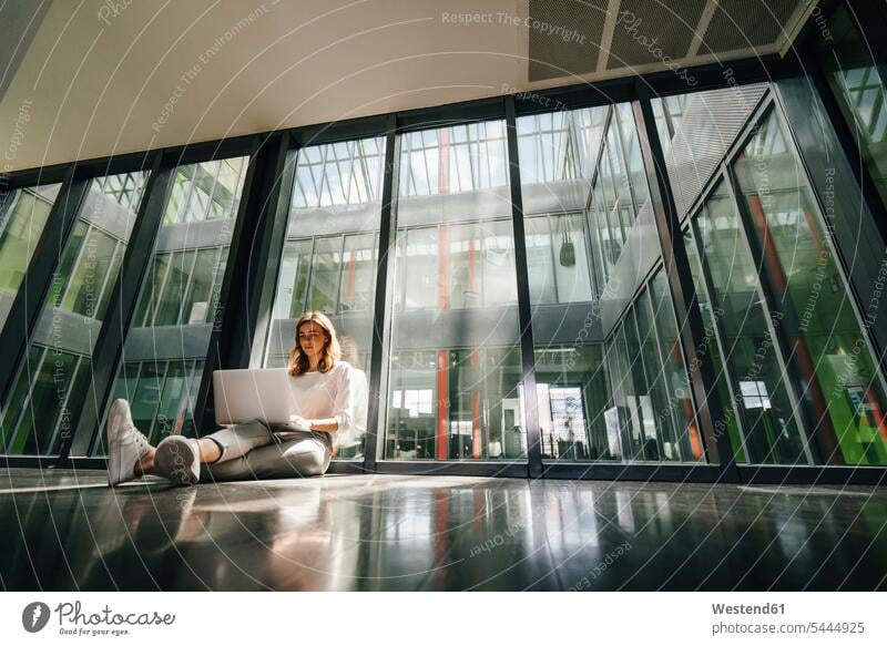 Geschäftsfrau sitzt am Boden in einem leeren Büro und benutzt einen Laptop Allein alleine einzeln sitzen sitzend auf dem Boden sitzen auf dem Boden sitzend