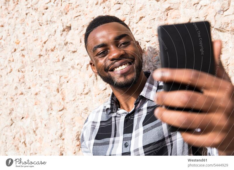 Porträt eines lächelnden jungen Mannes, der ein Selfie mit einem Mobiltelefon macht Männer männlich Selfies Smartphone iPhone Smartphones Erwachsener erwachsen