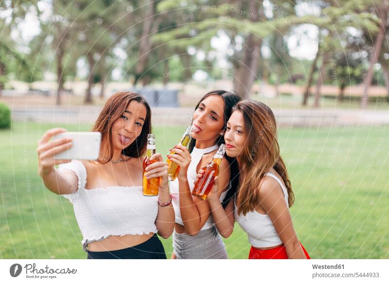 Verspielte Freunde in einem Park, die Bier trinken und ein Selfie machen Parkanlagen Parks halten Freundinnen Alkohol Alkoholische Getraenke