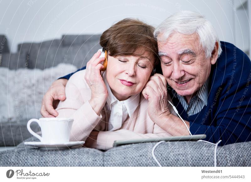 Älteres Ehepaar liegt auf dem Sofa und hört Musik von einem digitalen Tablet liegen liegend Senioren alte ältere Tablet Computer Tablet-PC Tablet PC iPad