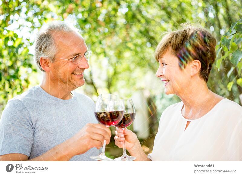 Lächelndes älteres Paar, das im Freien Rotweingläser klimpert lächeln Pärchen Paare Partnerschaft Wein Weine Mensch Menschen Leute People Personen Alkohol