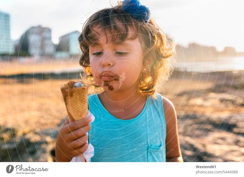 Porträt eines kleinen Mädchens, das bei Sonnenuntergang am Strand Schokoladeneis isst weiblich Portrait Porträts Portraits Eis Speiseeis Kind Kinder Kids Mensch