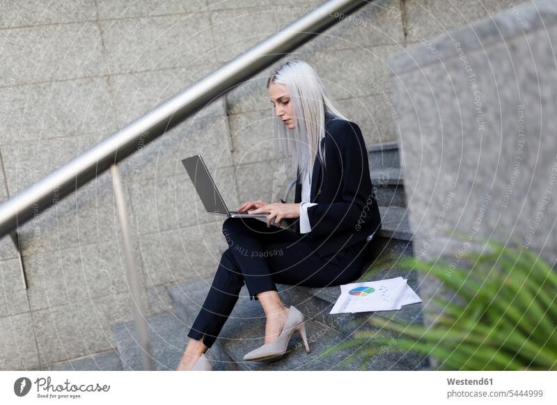 Junge Geschäftsfrau, die in der Stadt auf einer Treppe sitzt und einen Laptop benutzt Notebook Laptops Notebooks Geschäftsfrauen Businesswomen Businessfrauen
