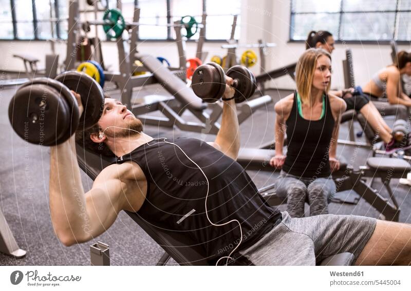 Junger Mann übt mit Hanteln im Fitnessstudio Gewicht Gewichte fit trainieren Gesundheit gesund Gewichtheben junge Frau junge Frauen junger Mann junge Männer