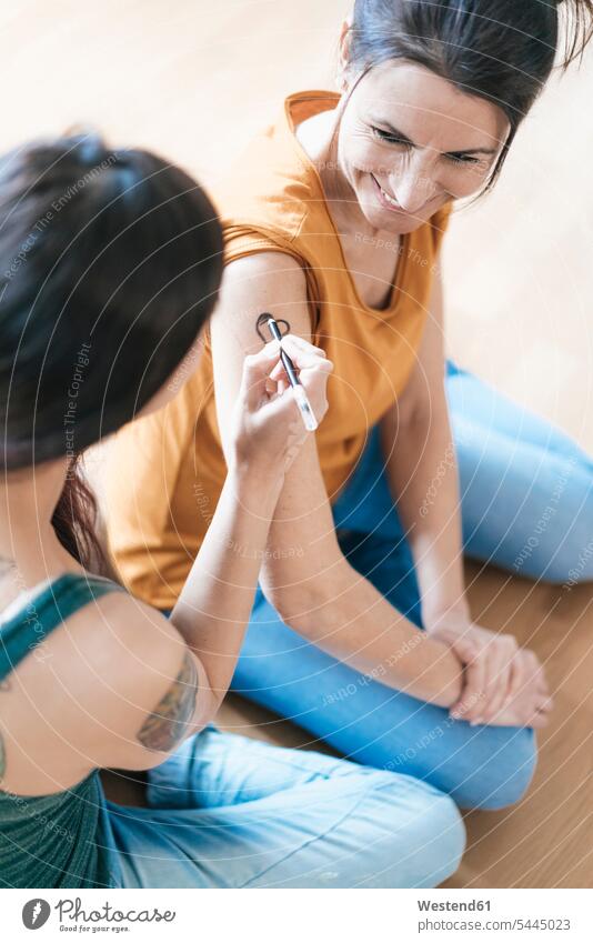 Frau malt Tätowierung auf den Arm einer anderen Frau lächeln weiblich Frauen Tattoo Tätowierungen Tatoos Taetowierung Tattoos Taetowierungen Erwachsener