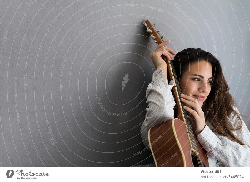 Porträt einer lächelnden jungen Frau mit Gitarre vor grauem Hintergrund Gitarren Portrait Porträts Portraits weiblich Frauen Saiteninstrument Saiteninstrumente
