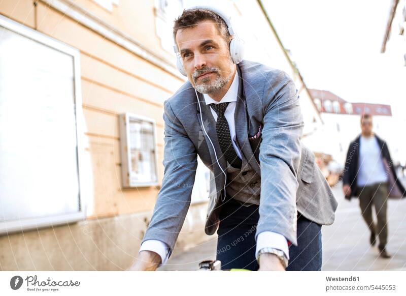 Älterer Geschäftsmann mit Kopfhörern beim Fahrradfahren in der Stadt Bikes Fahrräder Räder Rad Mann Männer männlich staedtisch städtisch Kopfhoerer Raeder