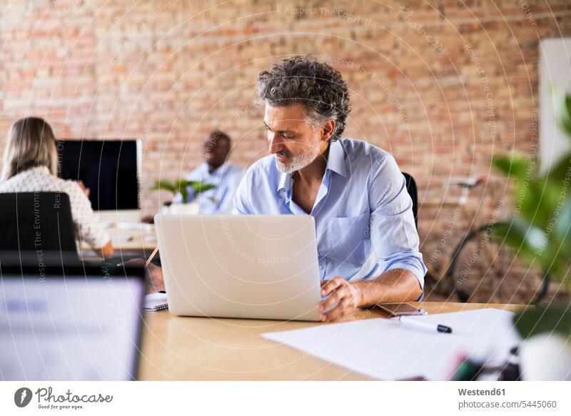 Geschäftsmann mit Laptop im Büro mit Kollegen im Hintergrund Schreibtisch Arbeitstisch Schreibtische arbeiten Businessmann Businessmänner Geschäftsmänner