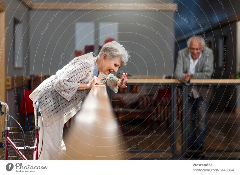 Senioren schauen vom Geländer herab, Frau winkt und lacht stehen stehend steht Altersheim Altenheim Seniorenheim beobachten zuschauen ansehen winken Seniorin