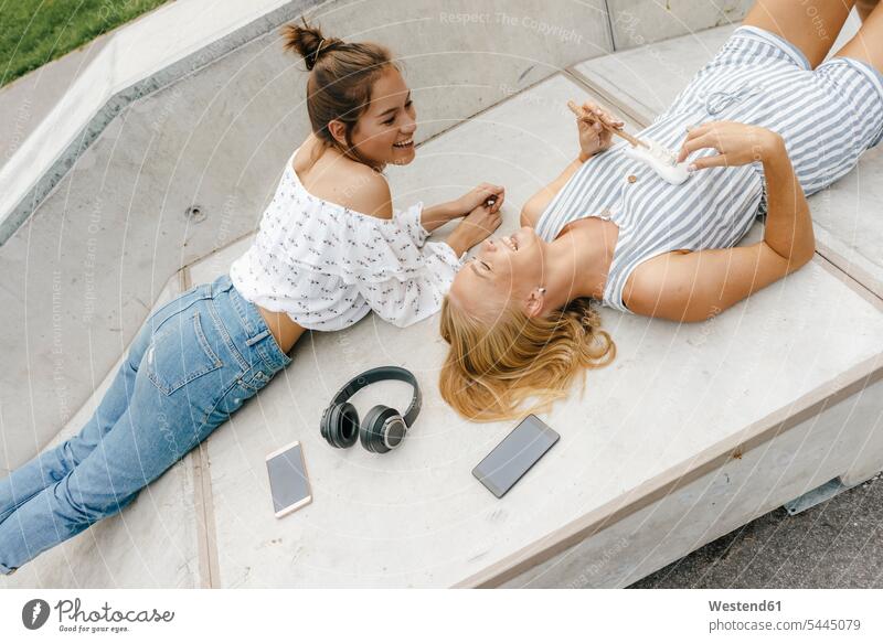 Zwei glückliche junge Frauen liegen auf einer Rampe in einem Skatepark und machen Musik Freundinnen liegend liegt Skateboardpark Skateboard-Park Skateboard Park