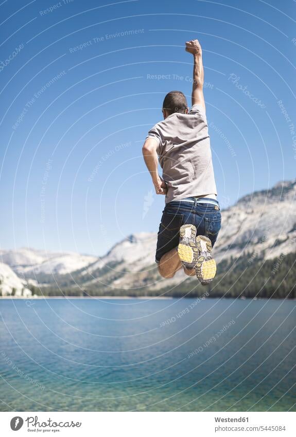 USA, Kalifornien, Yosemite National Park, Rückenansicht eines Mannes, der am Bergsee in die Luft springt Männer männlich See Seen springen hüpfen Erwachsener
