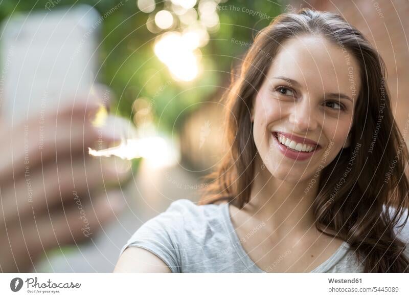 Porträt einer glücklichen jungen Frau im Freien, die ein Selfie macht lächeln Portrait Porträts Portraits Handy Mobiltelefon Handies Handys Mobiltelefone