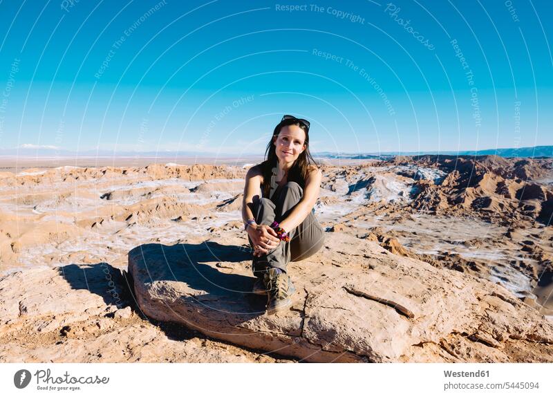 Chile, Atacama-Wüste, lächelnde Frau sitzt im Sonnenlicht auf einem Felsen weiblich Frauen Erwachsener erwachsen Mensch Menschen Leute People Personen sitzen