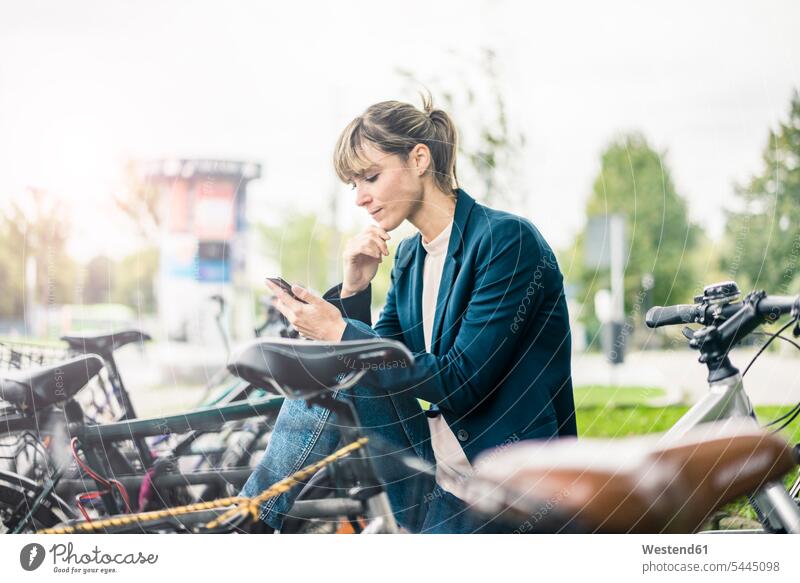 Geschäftsfrau benutzt Mobiltelefon im Freien, umgeben von Fahrrädern Geschäftsfrauen Businesswomen Businessfrauen Businesswoman Frau weiblich Frauen Fahrrad