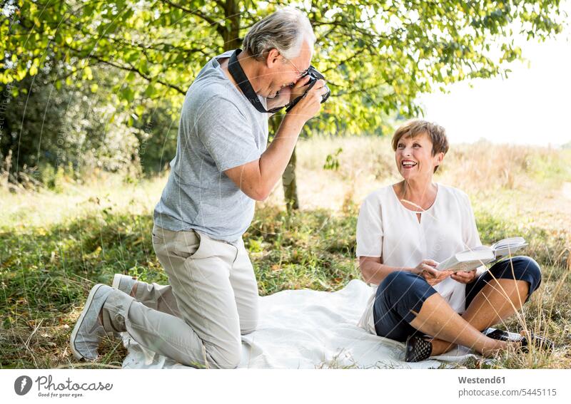 Glücklicher älterer Mann fotografiert seine Frau auf der Wiese Wiesen lächeln Fotoapparat Kamera Fotokamera fotografieren Paar Pärchen Paare Partnerschaft
